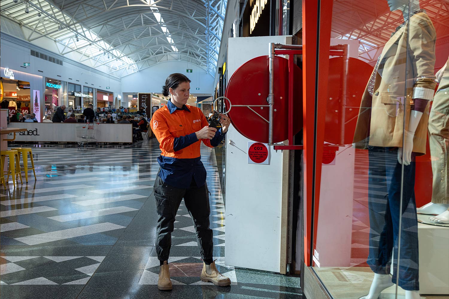 ARA Fire technician inspecting a fire panel inside a building. The technician is focused on ensuring the proper function of the fire detection system. The panel displays various controls and indicators related to fire safety management.